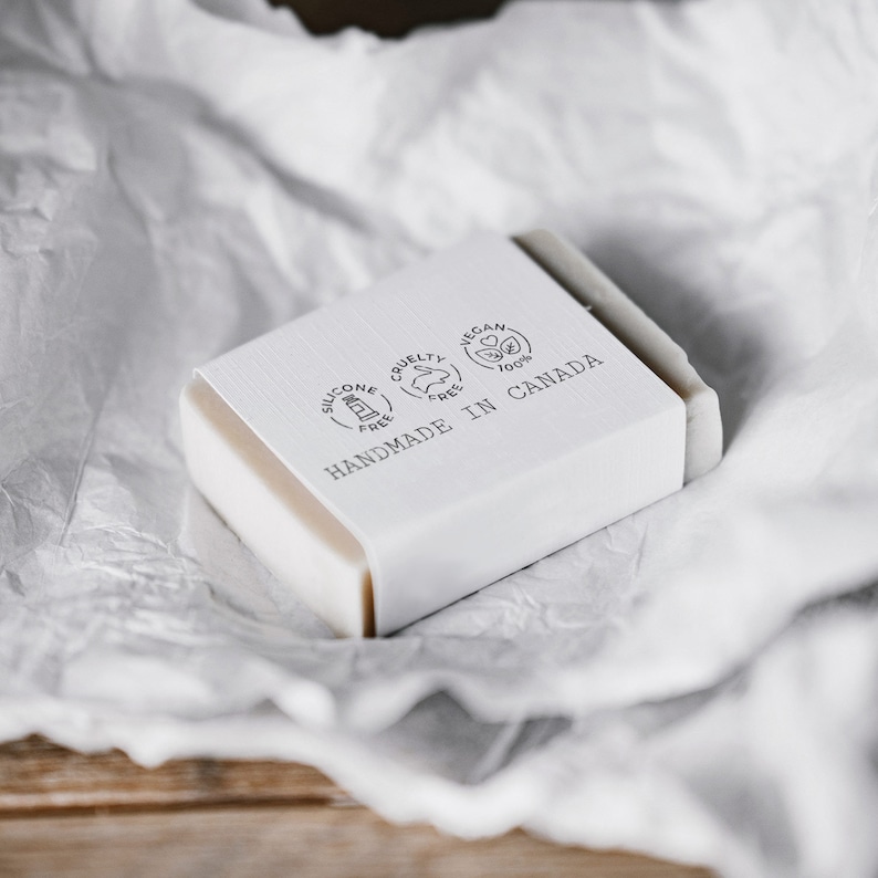 A handmade soap wrapped in a white paper band, stamped with a custom soap packaging stamp. The stamped design creates an elegant, natural branding for artisanal soaps. Perfect for eco-friendly soap makers using DIY labels and sustainable wrapping. The print is clear and crisp on the wrapping paper, ideal for handmade or solid shampoo packaging.