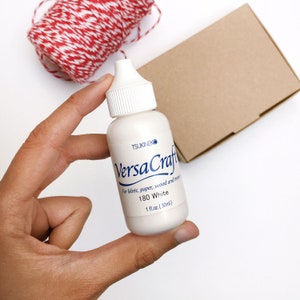 May include: A white bottle of VersaCraft 180 White fabric, paper, wood and more paint. The bottle is labeled with the brand name, product name, and size: 1 fl.oz. (30ml).