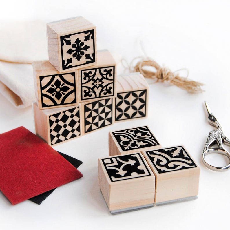 May include: Set of nine wooden stamps featuring black and white geometric tile designs. The stamps are arranged in a pyramid shape on a white surface.