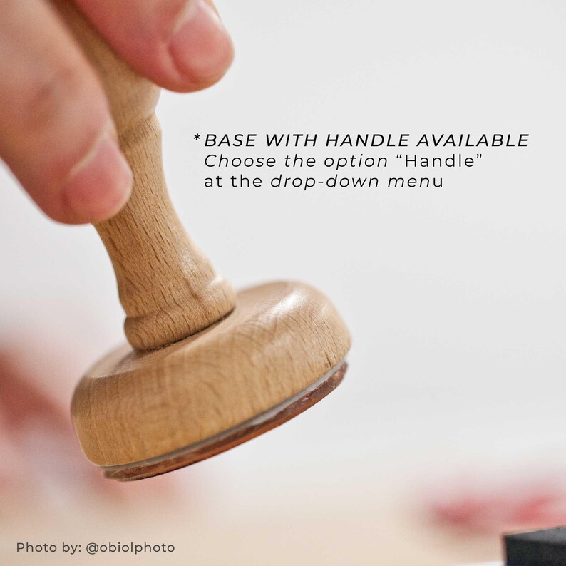 Op de afbeelding: Een houten stempel met een afgeronde basis en handvat. De basis heeft een bruine rand. Tekst op de afbeelding luidt: "*BASE WITH HANDLE AVAILABLE Choose the option "Handle" at the drop-down menu."