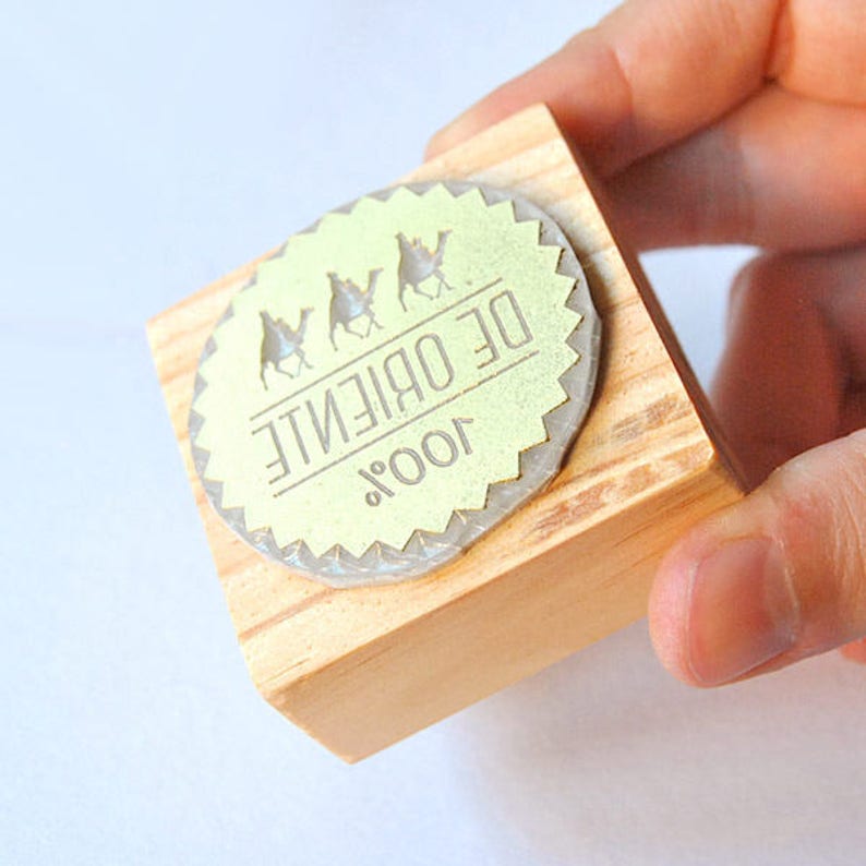 May include: A wooden block stamp with a round, green label that says "100% DE ORIENTE" and features three camel silhouettes.