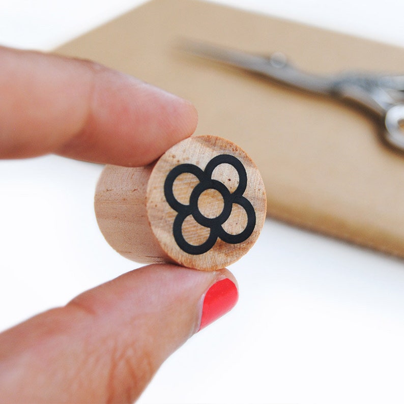 May include: A wooden stamp with a black and white design of a flower with five petals. The flower is a stylized design with five circles.