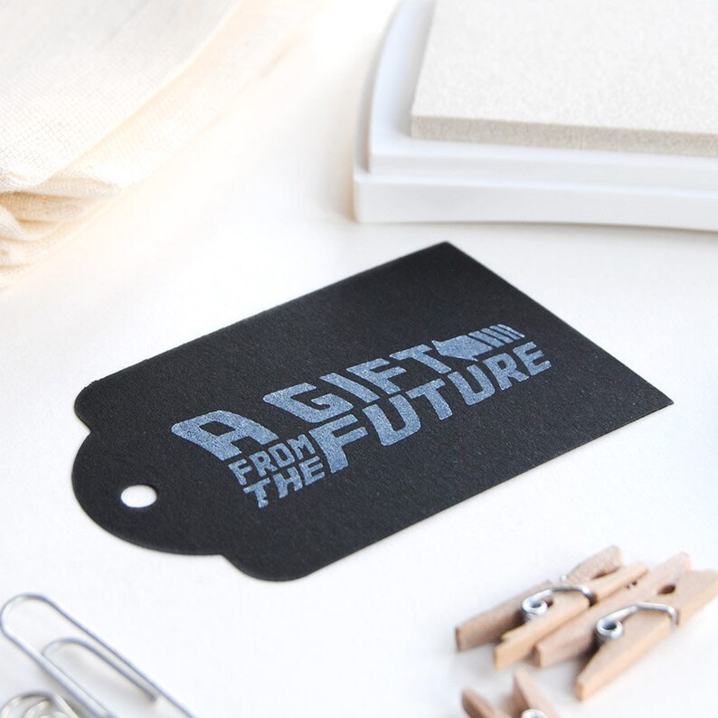 May include: A black gift tag with the text "A Gift From The Future" in silver lettering.
