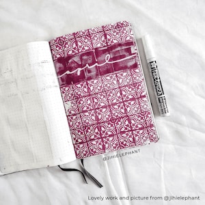 Puede incluir: Un cuaderno abierto con una p&aacute;gina de patr&oacute;n rosa y blanco. La p&aacute;gina tiene un dise&ntilde;o blanco de un patr&oacute;n repetido de cuadrados con un dise&ntilde;o floral dentro de cada cuadrado. La palabra "home" est&aacute; escrita en blanco en la p&aacute;gina. Un marcador de pintura blanco est&aacute; acostado junto al cuaderno. El cuaderno tiene el texto "@jhiieiephant" escrito en la esquina inferior derecha.