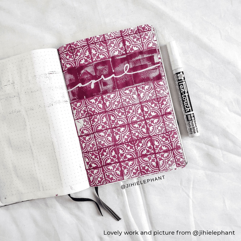 Puede incluir: Un cuaderno abierto con una p&aacute;gina de patr&oacute;n rosa y blanco. La p&aacute;gina tiene un dise&ntilde;o blanco de un patr&oacute;n repetido de cuadrados con un dise&ntilde;o floral dentro de cada cuadrado. La palabra "home" est&aacute; escrita en blanco en la p&aacute;gina. Un marcador de pintura blanco est&aacute; acostado junto al cuaderno. El cuaderno tiene el texto "@jhiieiephant" escrito en la esquina inferior derecha.