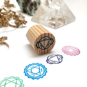 Puede incluir: Sello de madera con un diseño en blanco y negro del tercer chakra, también conocido como el chakra del plexo solar. El sello está sobre una superficie blanca con varios sellos de chakra en diferentes colores.