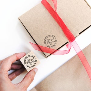 A small rubber stamp with a minimalist turtle design is held in hand, with its stamped impression on a cardboard box, demonstrating how it can be used to add an eco-friendly touch to shipping materials. This stamp is ideal for businesses that focus on sustainability and want to reinforce their environmental commitment. It’s perfect for stamping paper, packaging, and plastic-free products while spreading awareness about protecting marine life.