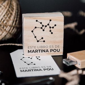 Könnte beinhalten: Ein Stempel aus Holz mit einem schwarzen Sternbild-Design und dem Text "ESTE LIBRO ES DE MARTINA POU".