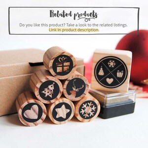 May include: A set of eight wooden Christmas stamps with various designs, including a Christmas tree, a reindeer, a star, a snowflake, a heart, a gift box, and a snowflake with a heart, a Christmas tree, and a gift box. The stamps are arranged in a pyramid shape on a white surface. There is also a black ink pad.