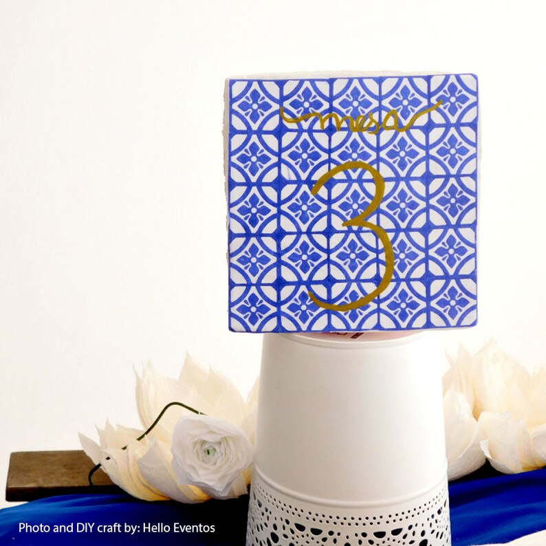 May include: Blue and white patterned tile with a gold number 3 and the word "mesa" written in gold cursive. The tile is sitting on a white stand with a lace pattern.