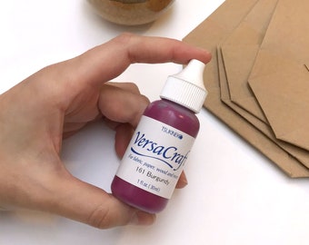 May include: A 1 fl. oz. (30 ml) bottle of VersaCraft ink in the color Burgundy. The bottle is labeled with the brand name Tsukineko and the ink is for fabric, paper, wood, and more.