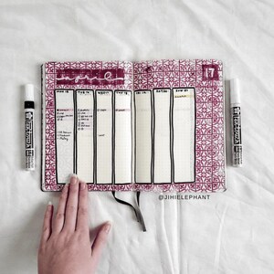 May include: A weekly planner with a pink and white patterned cover. The planner is open to the week of June 17th. The planner has a grid layout with spaces for each day of the week. The planner is labeled with the word "June" and the number "17".