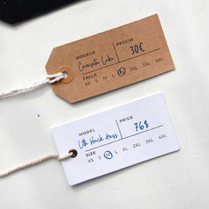 May include: Two clothing tags with handwritten text. The brown tag says "Camiseta Luke" and "30&euro;" with size options XS to 4XL. The white tag says "Little black dress" and "76$" with size options XS to 4XL.