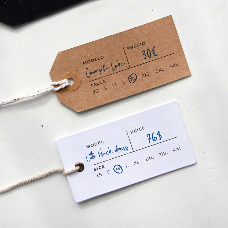 May include: Two clothing tags with handwritten text. The brown tag says "Camiseta Luke" and "30&euro;" with size options XS to 4XL. The white tag says "Little black dress" and "76$" with size options XS to 4XL.
