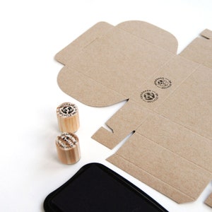 Close-up of mini rubber stamps printed on a cardboard box, demonstrating how the "100% Paper Recycle" stamp enhances eco-conscious packaging. The crisp imprint on recyclable material highlights the importance of reducing plastic waste in shipping. This small yet impactful tool is perfect for brands committed to sustainability and plastic-free packaging.