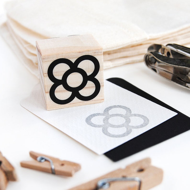 May include: A wooden stamp with a black and white flower design. The flower has six petals and a circle in the center. The stamp is sitting on a white surface.