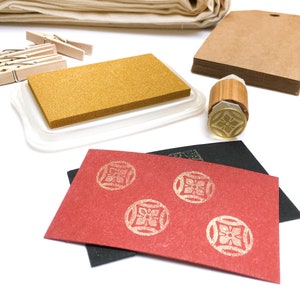 May include: A gold ink pad with a red card with gold stamps of a geometric design. The stamps are in a circle shape.