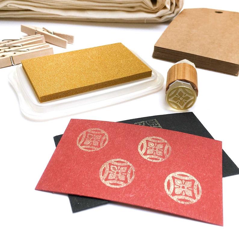 May include: A gold ink pad with a red card with gold stamps of a geometric design. The stamps are in a circle shape.