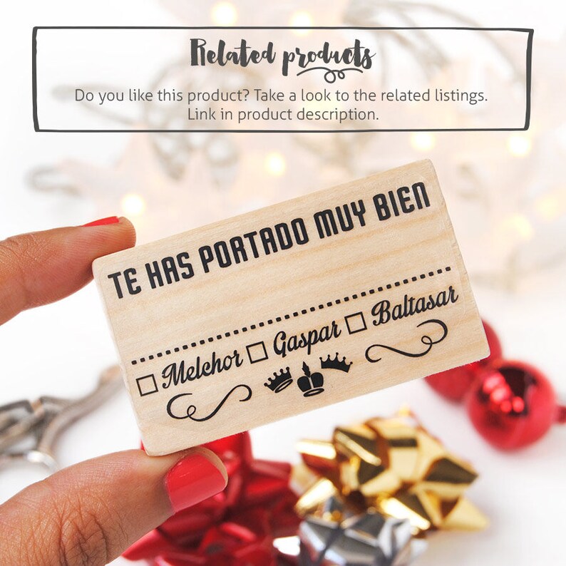 May include: Wooden stamp with the text "Te has portado muy bien" (You have behaved very well) and a checklist with the names of the three Wise Men: Melchior, Gaspar, and Baltasar. The stamp is held in a hand against a background of red and gold gift wrap.