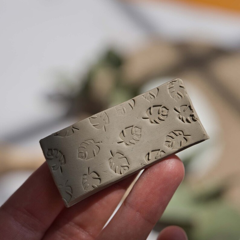 May include: A light brown rectangular clay tile with a pattern of embossed leaf shapes.