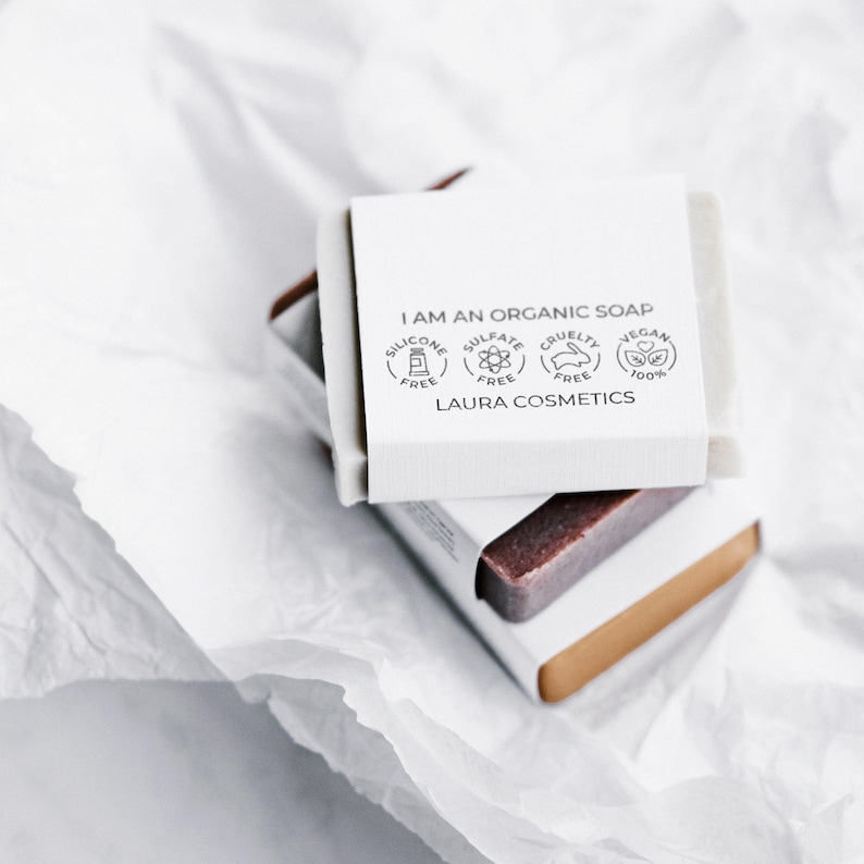 A stack of three handmade soaps, photographed from above, with the top soap featuring a custom soap stamp. The stamped design is visible on the soap's white paper band, showcasing a minimalist and professional branding solution for natural and handmade soap makers. The image highlights the clean and modern look of DIY stamped soap packaging.
