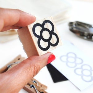 May include: A wooden stamp with a black and white flower design. The flower has five petals and a circle in the center.