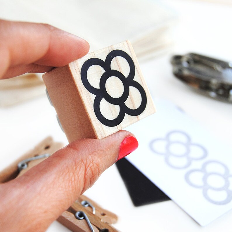 May include: A wooden stamp with a black and white flower design. The flower has five petals and a circle in the center.