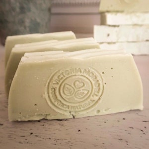 May include: Four bars of pale green soap with a white top layer. The bottom bar has a round stamp with the text "VICTORIA AMORE COSMETICA NATURAL" in a circle.
