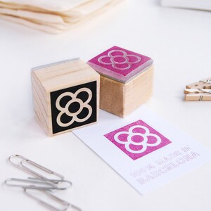 May include: Two wooden stamps with a black and white flower design and a pink flower design. The stamps are on a white surface with a card that says "100% MADE IN BARCELONA".