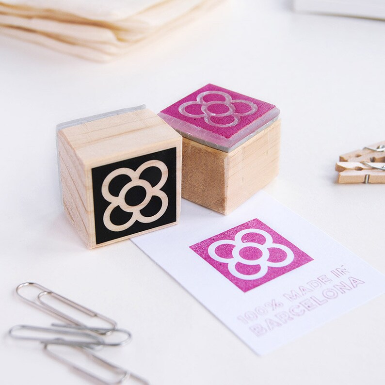 May include: Two wooden stamps with a black and white flower design and a pink flower design. The stamps are on a white surface with a card that says "100% MADE IN BARCELONA".