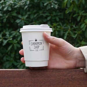 May include: White to-go cup with a black logo that says "Cinnamon Shop Teas" and a small image of a teapot.