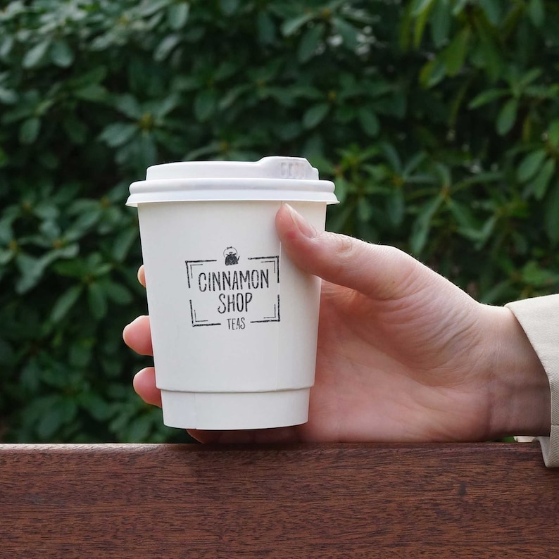 May include: White to-go cup with a black logo that says "Cinnamon Shop Teas" and a small image of a teapot.