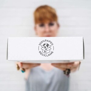 A woman holds a white box facing the camera, with the 100% Paper Recycle stamp printed on the side. This image highlights how the stamp helps businesses clearly communicate their commitment to sustainability. The simple, eco-conscious marking encourages customers to recycle packaging and support waste-free shipping practices. Ideal for online shops and eco-friendly brands.