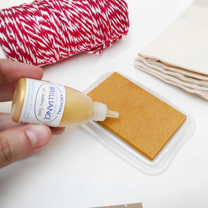 May include: A gold ink pad with a clear plastic cover and a bottle of gold archival ink labeled "Archival Brilliance Pigment Ink Refill 91 Galaxy Gold".