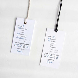 May include: Two white fabric care labels with black string. The label on the left says "Talla M" and lists the fabric composition in Spanish. The label on the right says "Size XL" and lists the fabric composition in English. Both labels include washing instructions and say "Hecho en Sevilla" and "Made in Sevilla" respectively.