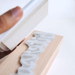May include: A close-up of a wooden block with the word "inspiration" carved into it. A white sponge is being used to rub ink off the block.