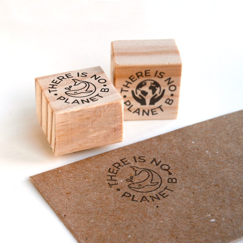 Two eco-friendly rubber stamps featuring a minimalist whale and hands holding the Earth designs. One stamp is pressed onto a kraft envelope, showing how it creates a clean and professional eco-conscious detail for small business packaging. These stamps are perfect for brands that want to highlight sustainability on their shipping materials, adding a handmade touch to paper envelopes, boxes, and plastic-free shipments while spreading an environmental message.