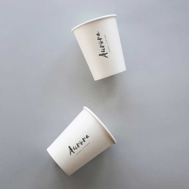 May include: Two white paper cups with black text that reads "Aurora" and "PARA LLEVAR" on them. The cups are on a gray background.