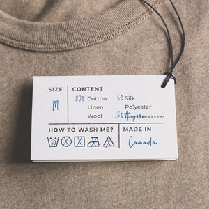 May include: A white clothing tag with black text and symbols. The tag lists the size as "M" and the content as 80% cotton, 5% silk, linen, and 15% Angora. The tag also includes instructions for washing the garment and states that it was made in Canada.