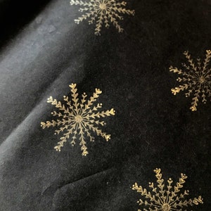 May include: Black fabric with a repeating pattern of gold snowflakes.
