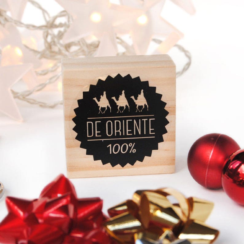 May include: A wooden stamp with a black and white design. The design features three camels with riders and the text "DE ORIENTE 100%".