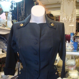 Op de afbeelding: Een donkerblauwe blazer met gouden knopen en een getailleerde pasvorm. De blazer heeft een kraag en lange mouwen. De blazer is op een mannequin.