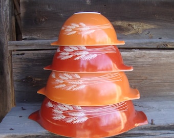 May include: A set of four nesting mixing bowls with a wheat design. The bowls are orange and red with white wheat stalks. The bowls are stacked on top of each other.