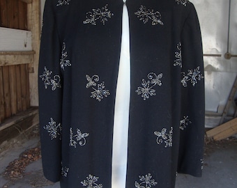 May include: A black cardigan with a beaded floral design. The cardigan has a shawl collar and a front closure.