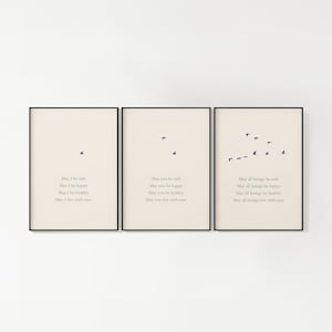 May include: Three framed prints with a beige background and black frames. Each print features a flock of birds flying in formation and a short poem about safety, happiness, health, and living with ease. The first print reads "May I be safe, May I be happy, May I be healthy, May I live with ease". The second print reads "May you be safe, May you be happy, May you be healthy, May you live with ease". The third print reads "May all beings be safe, May all beings be happy, May all beings be healthy, May all beings live with ease".