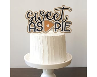 May include: A white cake with a brown and black cake topper that says "sweet as pie" with a brown pie slice graphic.