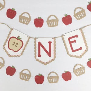 Peut inclure: Une banni&egrave;re sur le th&egrave;me de la pomme rouge et blanche avec le mot "ONE" en lettres rouges. La banni&egrave;re est d&eacute;cor&eacute;e de pommes rouges, de paniers bruns et d'un motif vichy blanc et rouge.