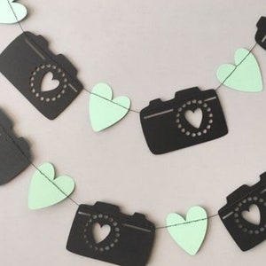 May include: A black and white camera and heart garland with mint green hearts. The garland is strung together with white string.