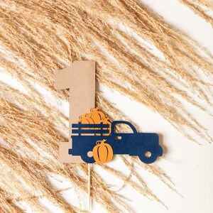 May include: A brown paper cutout of the number one with a blue truck carrying pumpkins. The truck is on a wooden stick.