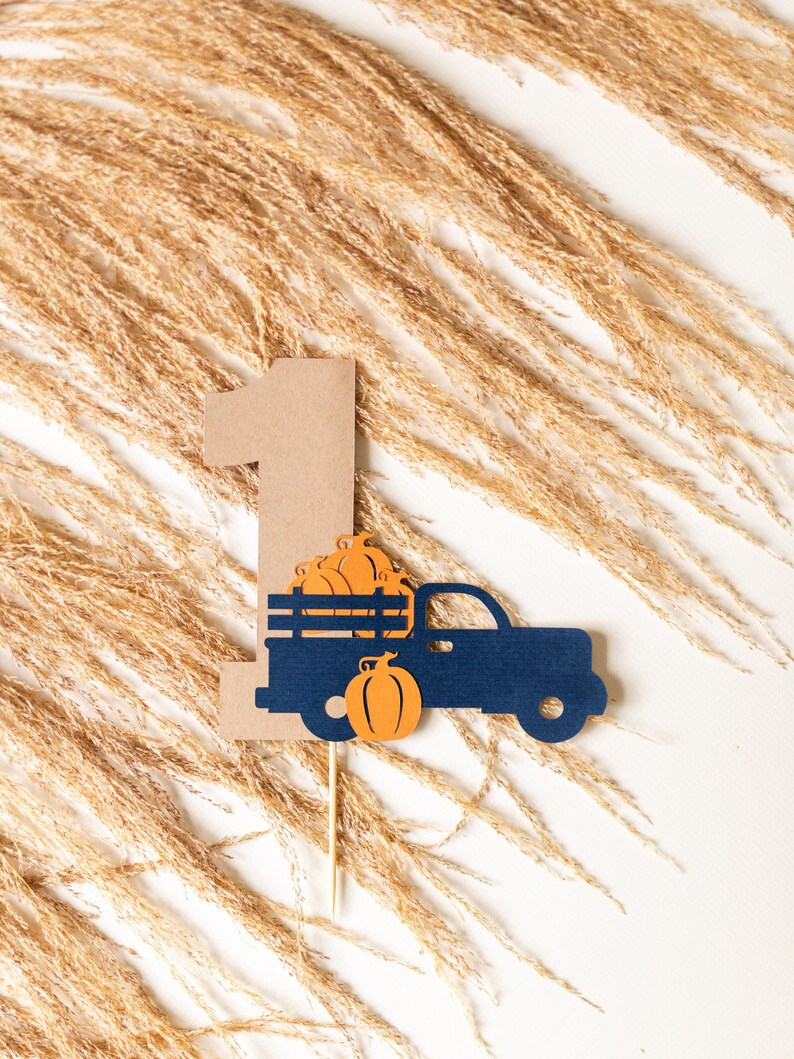 May include: A brown paper cutout of the number one with a blue truck carrying pumpkins. The truck is on a wooden stick.